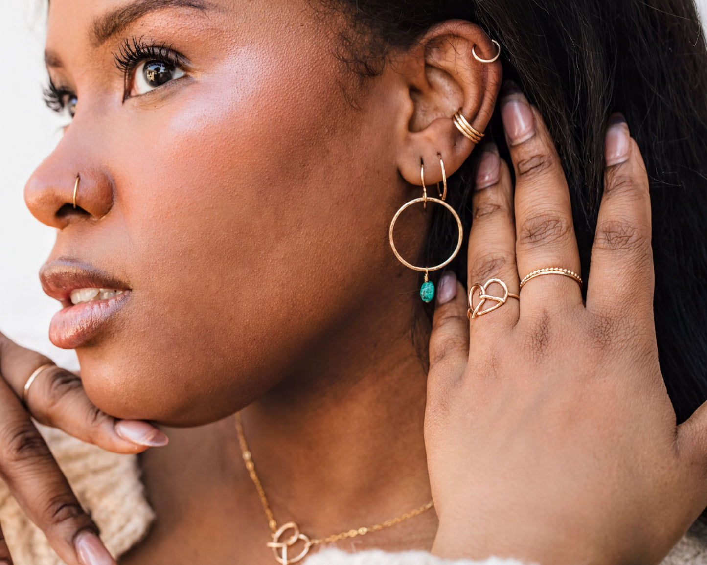 A close-up of a woman's face wearing multiple gold jewelry pieces, including earrings, rings, and a nose ring.