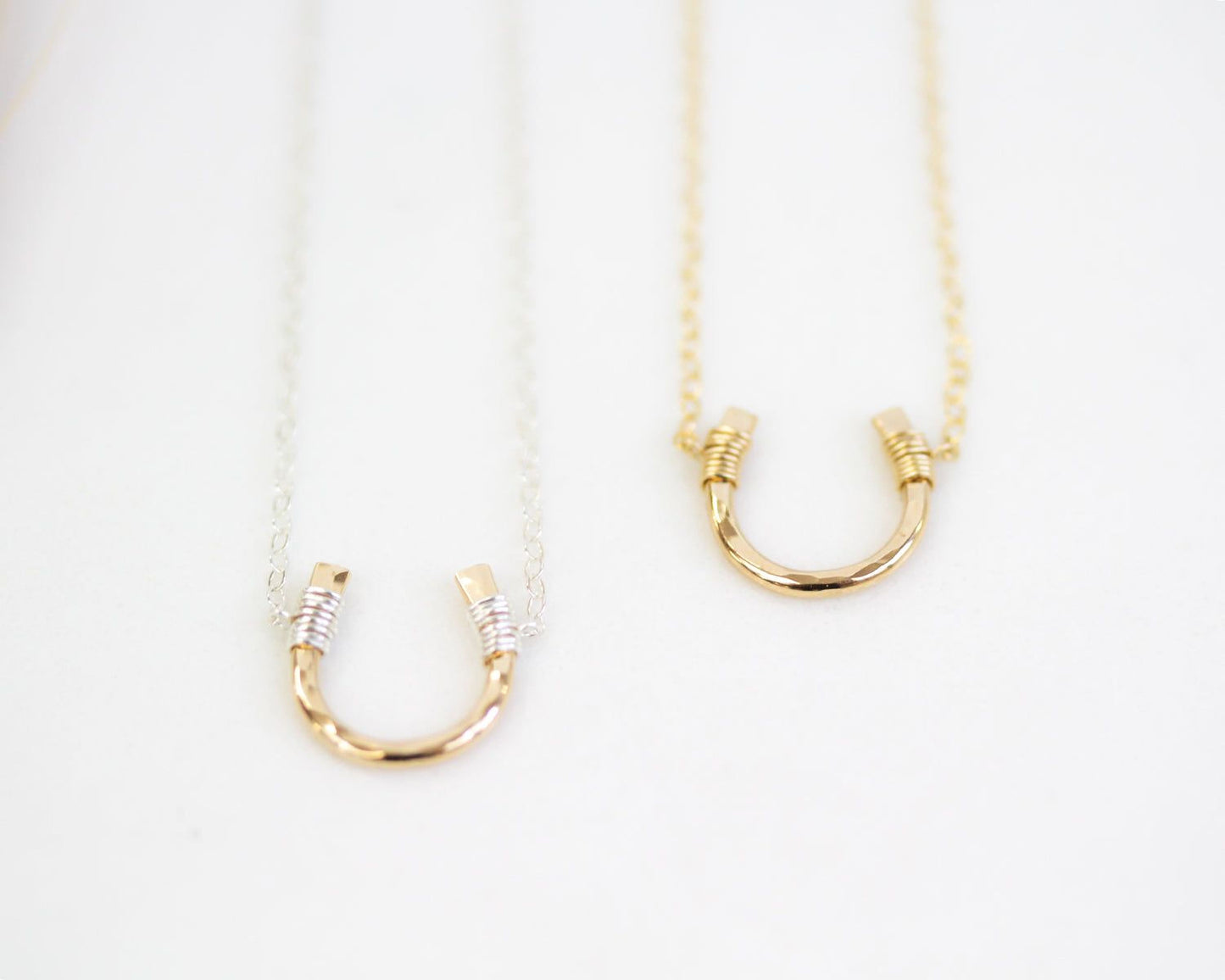 Two gold-colored necklaces with a horseshoe-shaped pendant are displayed against a white background.