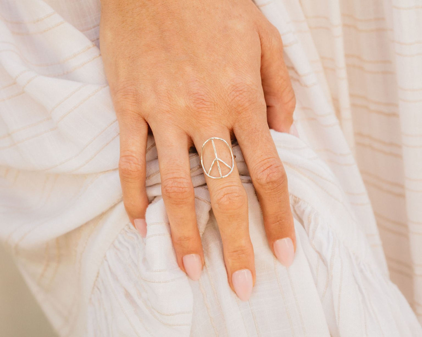 A close-up of a hand wearing a peace sign ring, with a white fabric or material in the background.