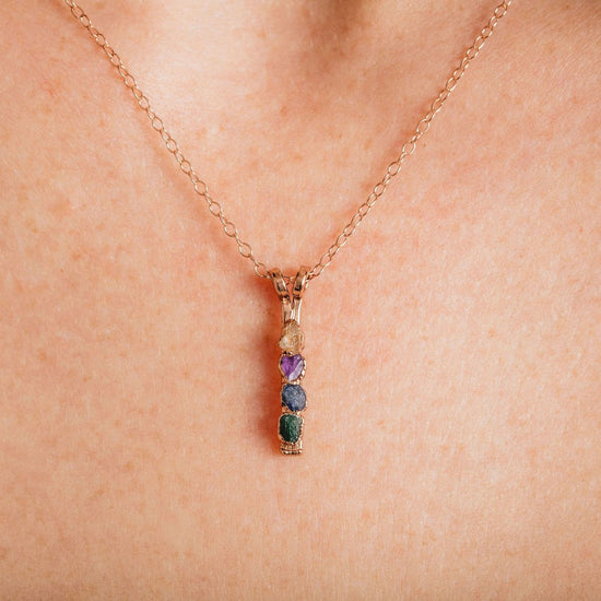 A close-up view of a delicate gold necklace with a pendant featuring a row of colorful gemstones.