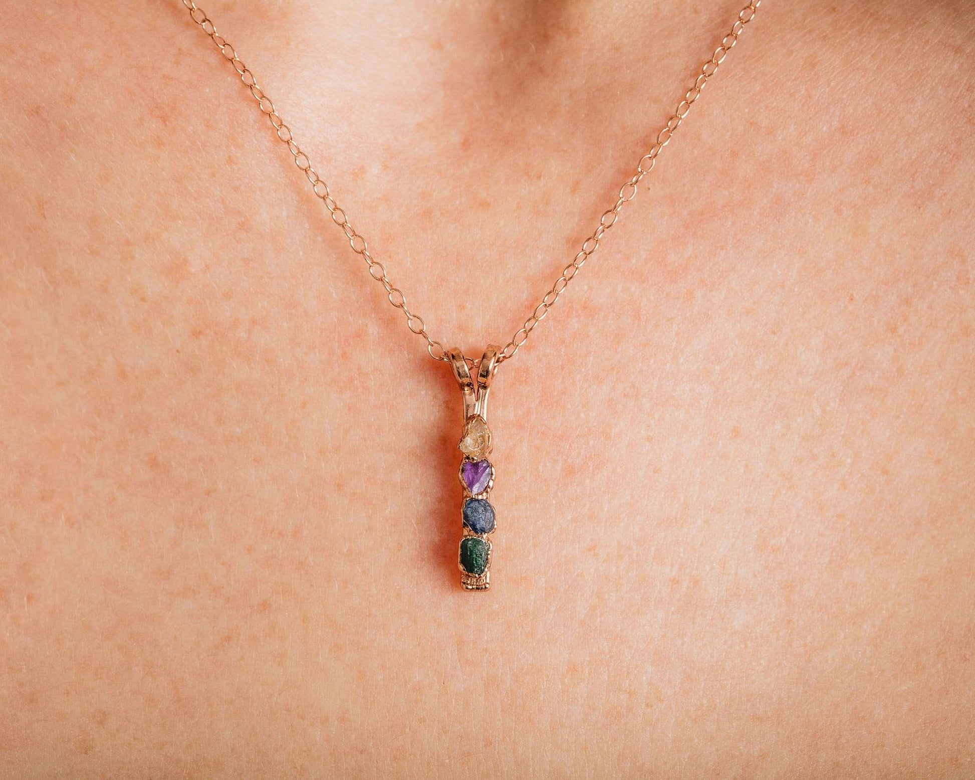 A close-up view of a delicate gold necklace with a pendant featuring a row of colorful gemstones.