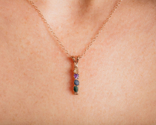 A close-up view of a delicate gold necklace with a pendant featuring a row of colorful gemstones.