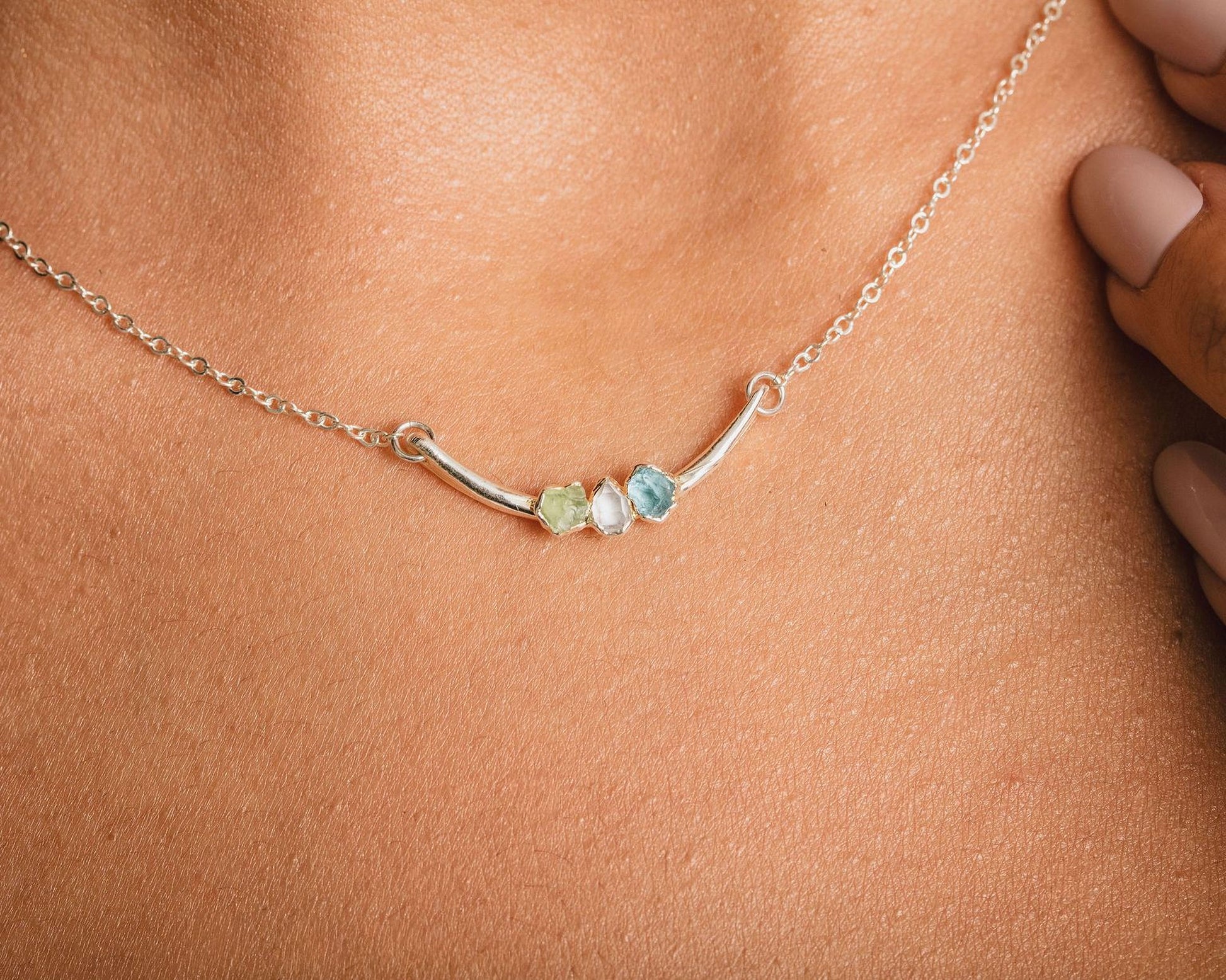 A close-up view of a silver necklace with three gemstones, including a blue gemstone, on a person's neck.