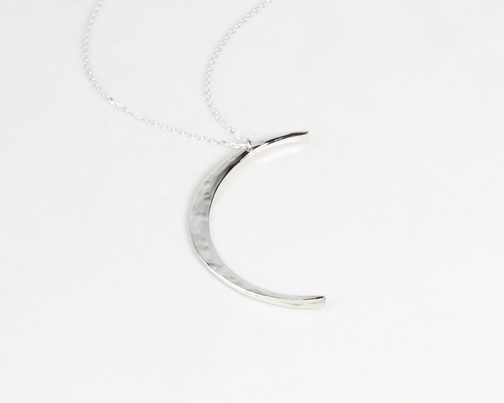Close up shows our Moon Necklace in Sterling Silver with delicate hand hammered texture. The Mystic Moon Necklace elevates celestial jewelry and beams with handcrafted quality. Each moon pendant is hand forged by our team of women artists.