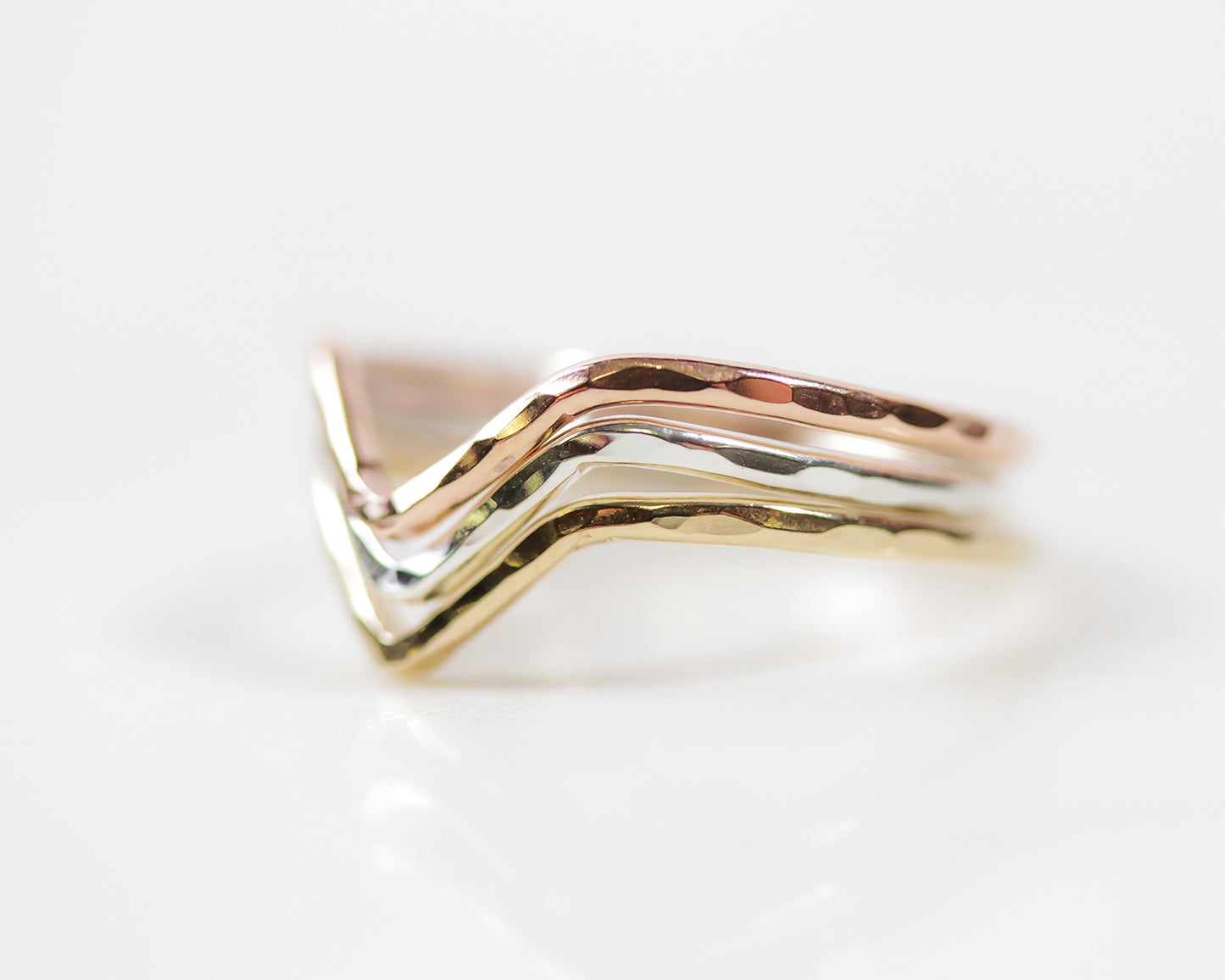 This minimalist V shaped ring is strong, bold, delicate and wearable. Image shows close up of the Chevron Ring in all metal selects, rose and gold fill and sterling. It shows the side of the band&#39;s hand hammered technique that makes it sparkle.