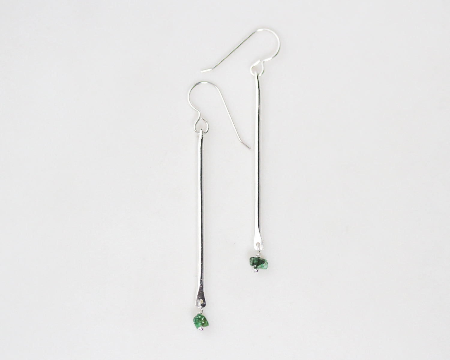 Close up image features our birthstone bar earrings in sterling silver with genuine emeralds falling delicately from the handmade bar earrings. Beautiful ear wires in sterling silver grace the bars. We hand hammered them to offer texture and bling.
