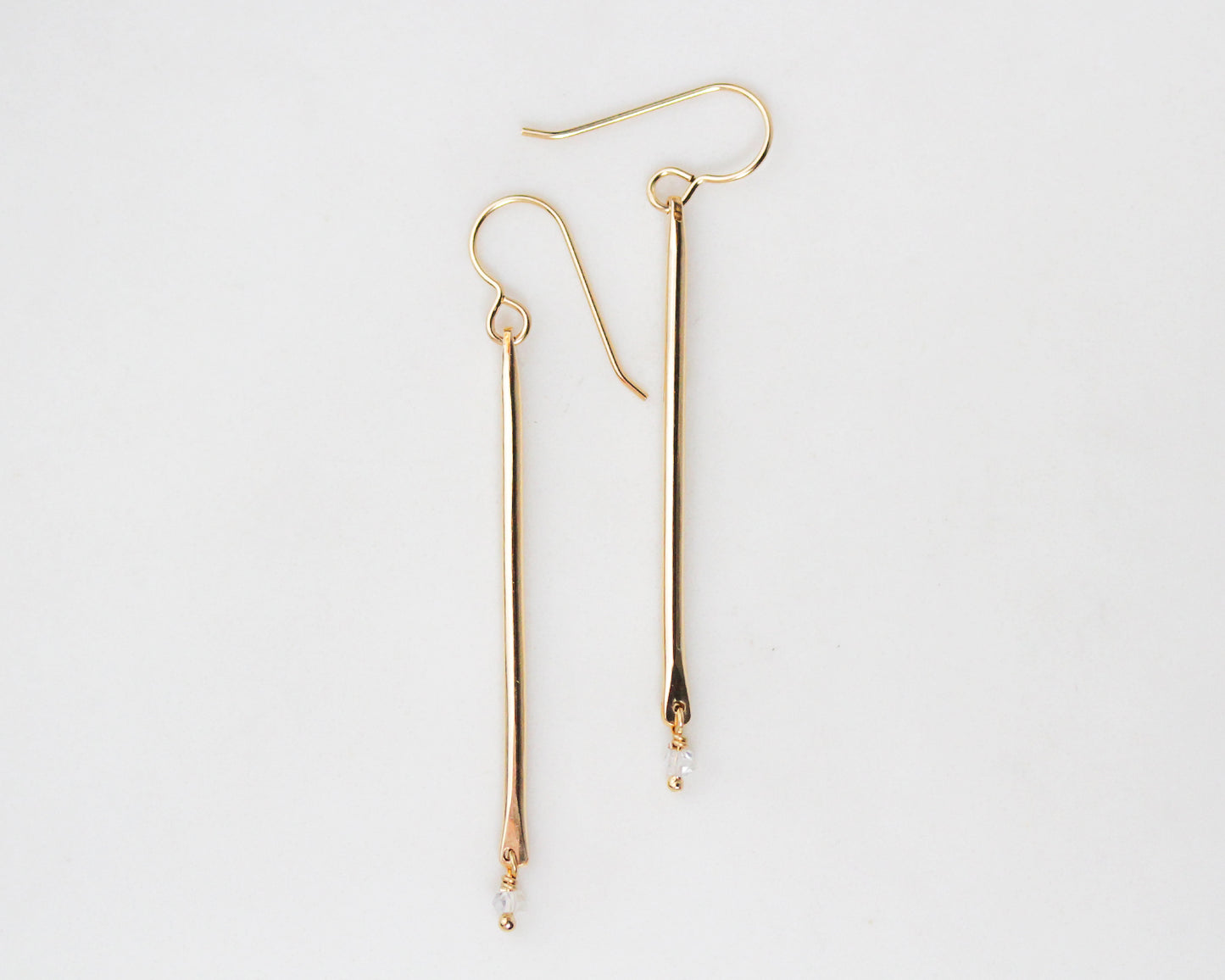 Image features our 14 karat yellow gold filled delicate and lightly hammered birthstone pendulum earrings. Featuring Herkimer diamonds, as the birthstone drop, these minimal earrings are the perfect gift for her and great for every day wear.
