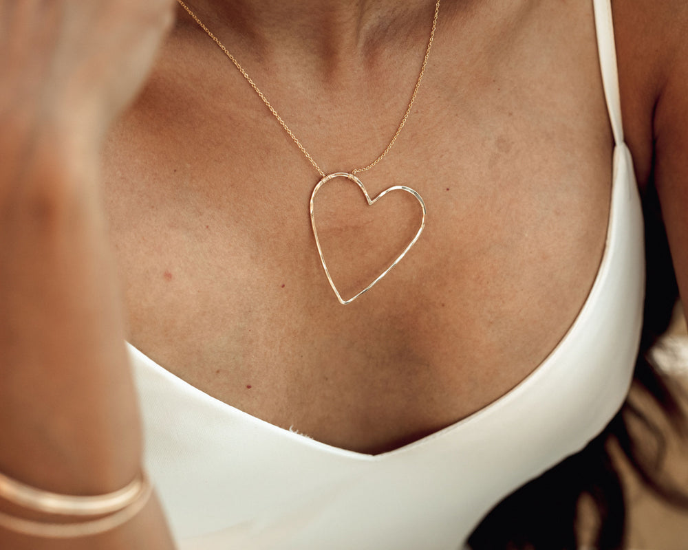Image shows close up on model wearing our 14 karat yellow gold filled sweet heart necklace. Whether given as a Valentines gift for her or a token of self love, this adorable and elevated heart necklace will resonate with sweethearts around the world.