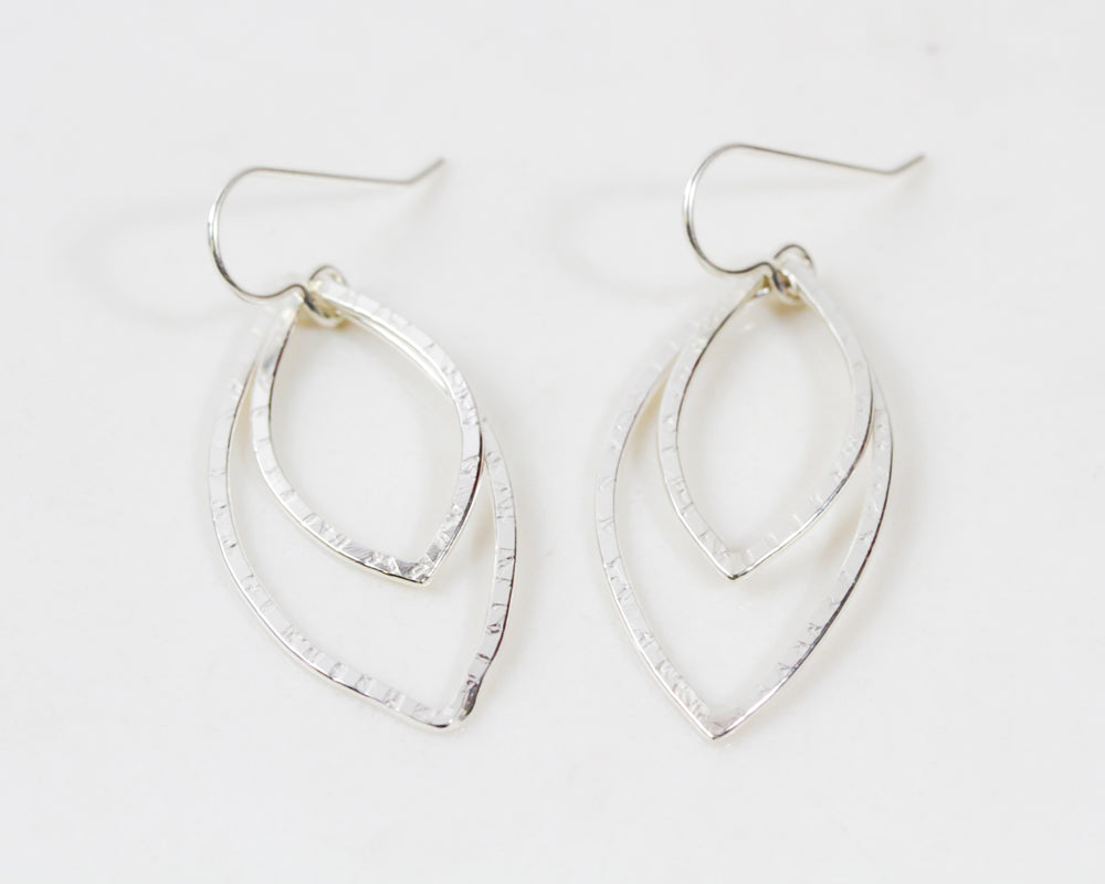 Close up shows the .925 sterling silver format. Two delicately handcrafted leaf shapes fall from sterling ear wires. The texture is subtle handmade and charming, denoting the veins of the leaf. Forged from high quality metal, the design is minimalist