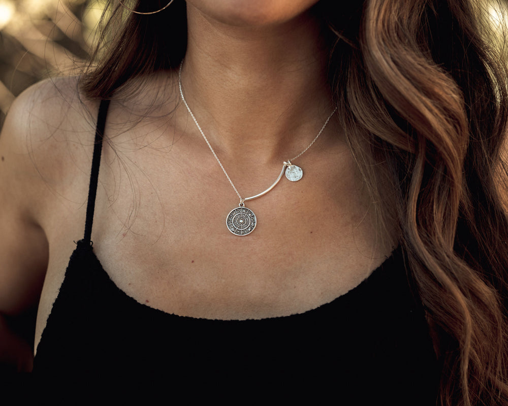 Image shows model wearing 16 inch Kismet Necklace. The larger, lower hanging celestial disc, is cast in fine detail with each sign of the zodiac, representing us all. The second disc is organically shaped with a rustic hammered texture.