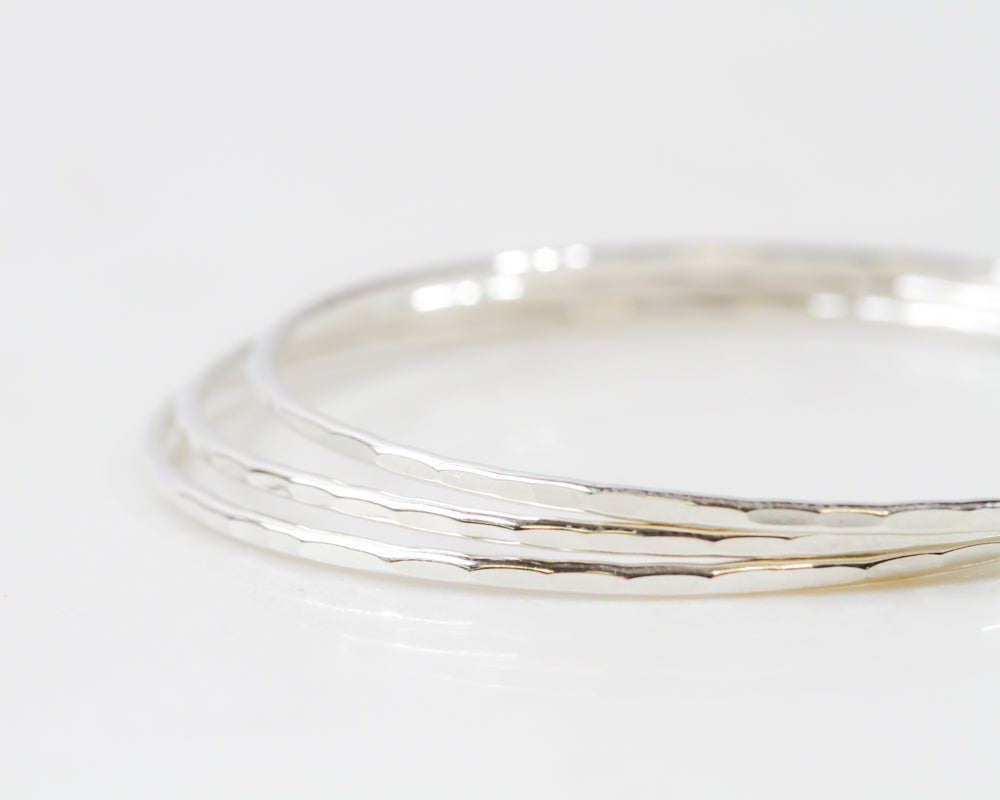 Image shows our handcrafted ultra thin sterling silver bangles. Each one is handmade in house and given a light texture to catch the sun. Beautiful, polished, shiny, each bangle bracelet width is 1/16 inch and can be worn individually or as a stack.