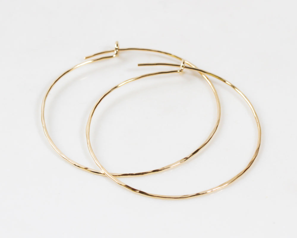 Image shows close up of our 3 inch 14 karat yellow gold filled hoop earrings. A delicate texture is hand hammered. All hand forged in our studio by a team of artisans who love what they do. Handmade in the USA.