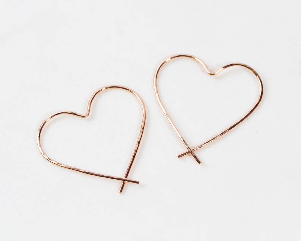 Image shows close up of our 14 karat rose gold filled slip in heart hoops. Our handmade Heart Hoop Earrings are hand forged from 18 gauge fine metal wire and lightly hammered for a twinkling texture. Perfect gift for her on Valentines Day.