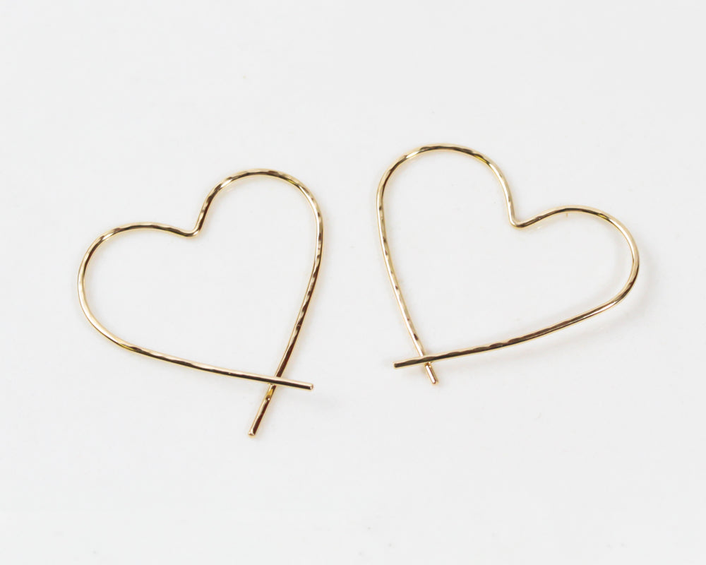 Image shows close up of our 14 karat yellow gold filled slip in heart hoops. Our handmade Heart Hoop Earrings are hand forged from 18 gauge fine metal wire and lightly hammered for a twinkling texture. Our Heart Hoops are a perfect symbol of love.