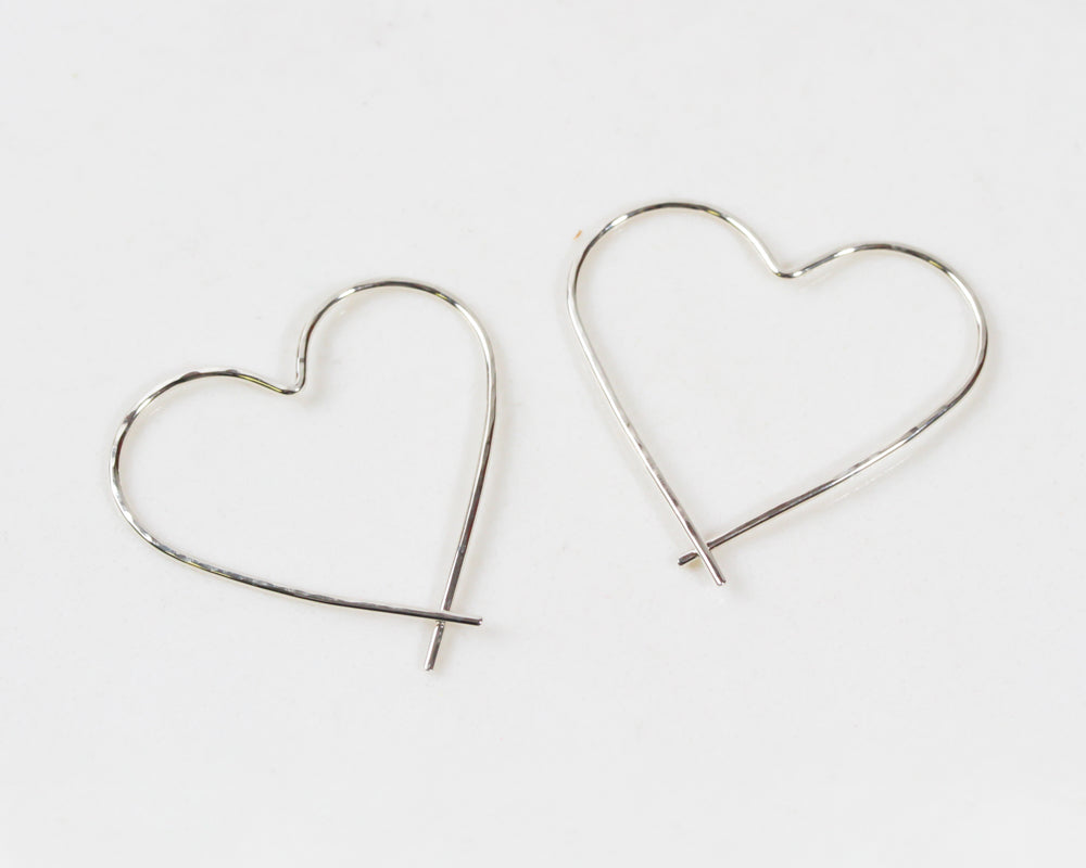 Image shows close up of our sterling silver heart hoops. Our handmade Heart Hoop Earrings are hand forged from 18 gauge fine metal wire and lightly hammered for a twinkling texture. The stunning hand craftsmanship is offered in weightless design.