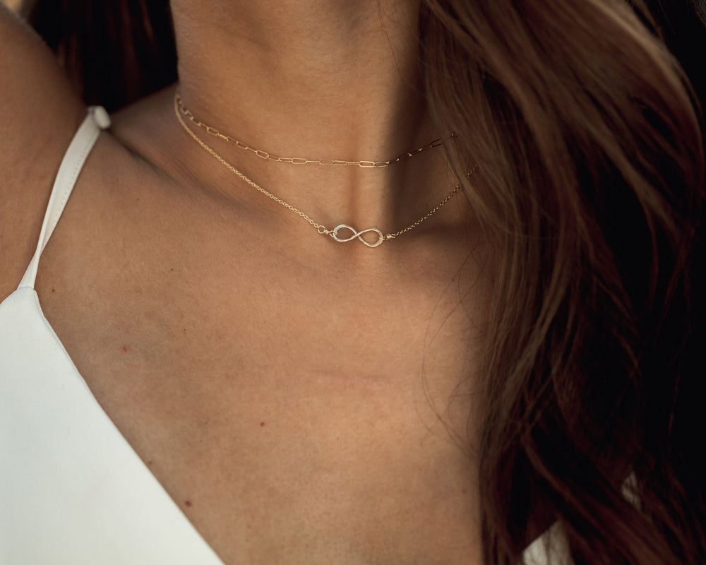 Image shows model wearing our delicate gold Infinity Symbol Necklace. The tiny infinity symbol is the perfect size for wearing everyday and layering with other necklaces. Made from 14 karat gold filled, this necklace is handmade in house.
